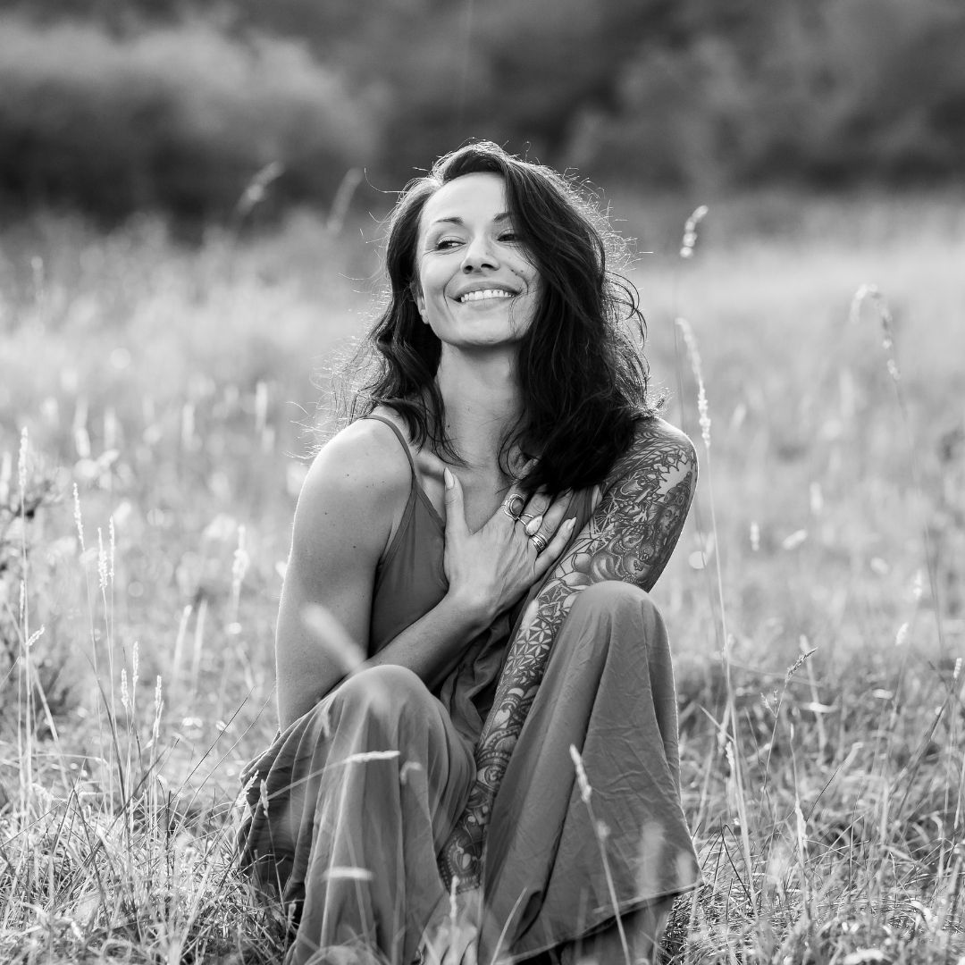 Woman smiling with hand on heart in a field, representing nervous system regulation and self-connection